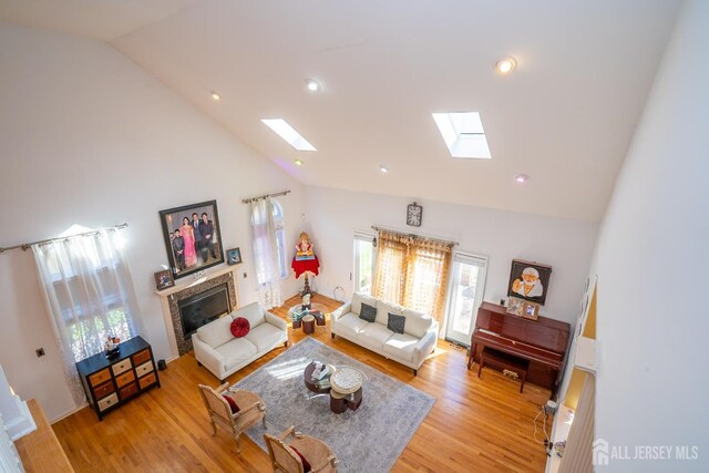 living room featuring a skylight, high vaulted ceiling, and light hardwood / wood-style flooring