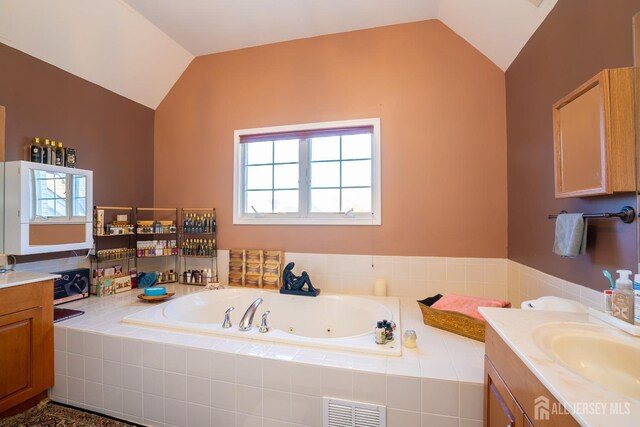 bathroom featuring vanity, vaulted ceiling, and tiled bath