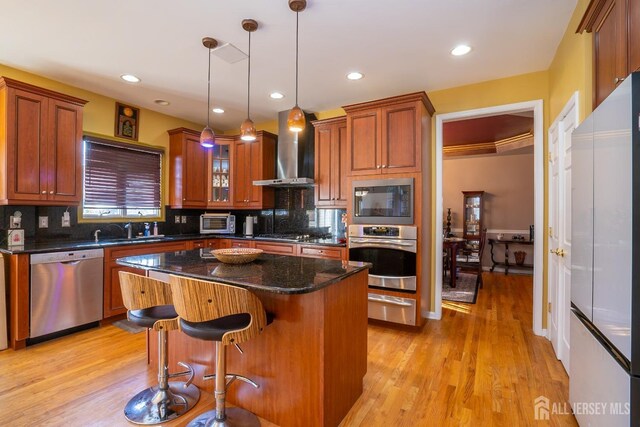 kitchen with a center island, appliances with stainless steel finishes, pendant lighting, dark stone counters, and wall chimney range hood