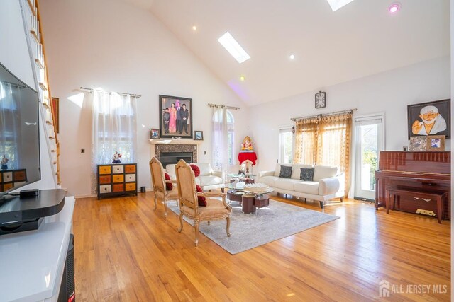 living room with a skylight, high vaulted ceiling, and light wood-type flooring