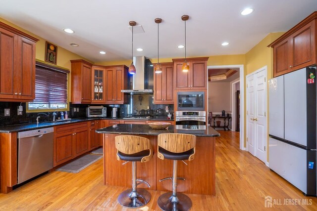 kitchen with wall chimney exhaust hood, a kitchen island, pendant lighting, stainless steel appliances, and backsplash