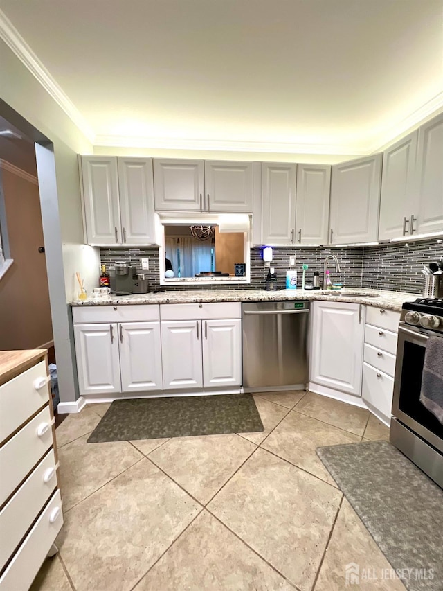 kitchen with appliances with stainless steel finishes, sink, white cabinets, ornamental molding, and light tile patterned floors