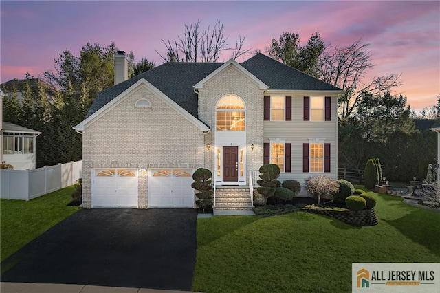 colonial inspired home with fence, a yard, a chimney, aphalt driveway, and brick siding