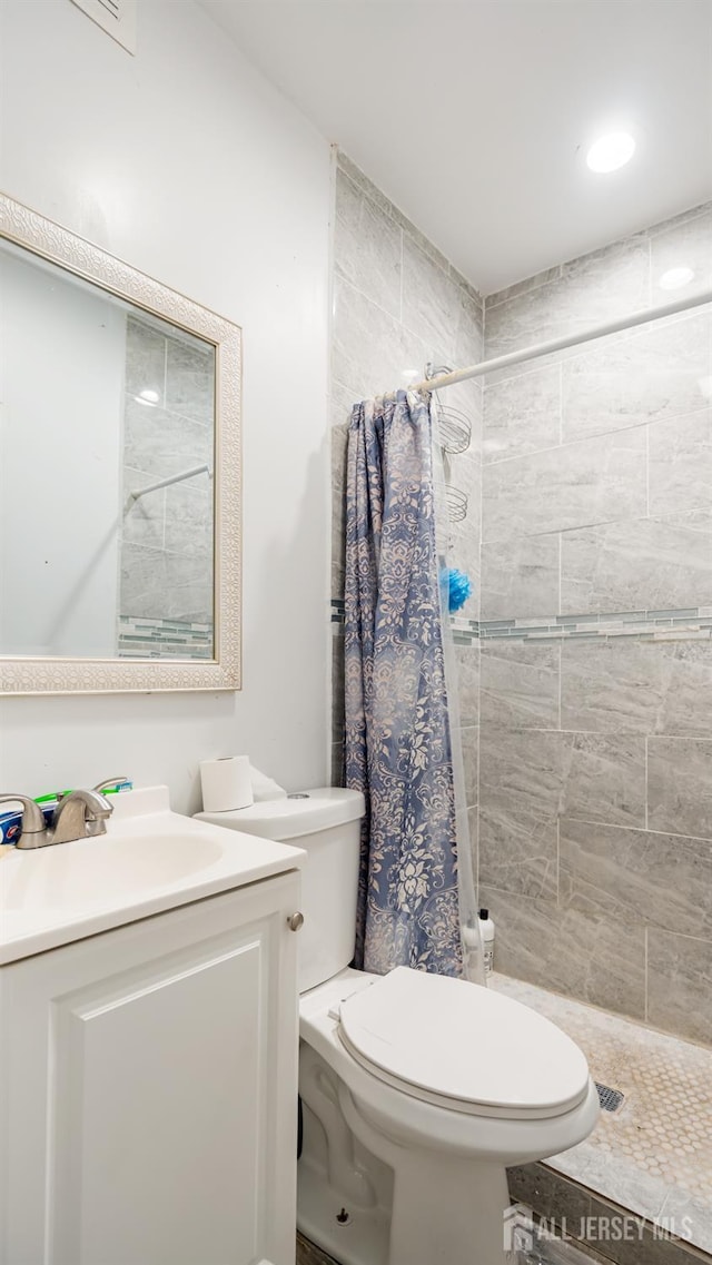 full bath featuring tiled shower, toilet, and vanity