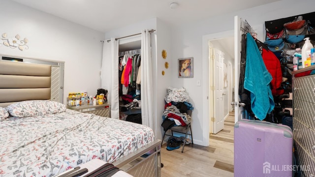 bedroom with light wood-style floors, a closet, a walk in closet, and baseboards