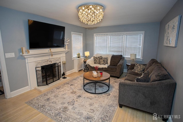 living room with an inviting chandelier, a stone fireplace, and light wood-type flooring