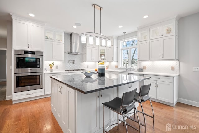 kitchen with white cabinets, wall chimney exhaust hood, light wood-type flooring, and stainless steel double oven