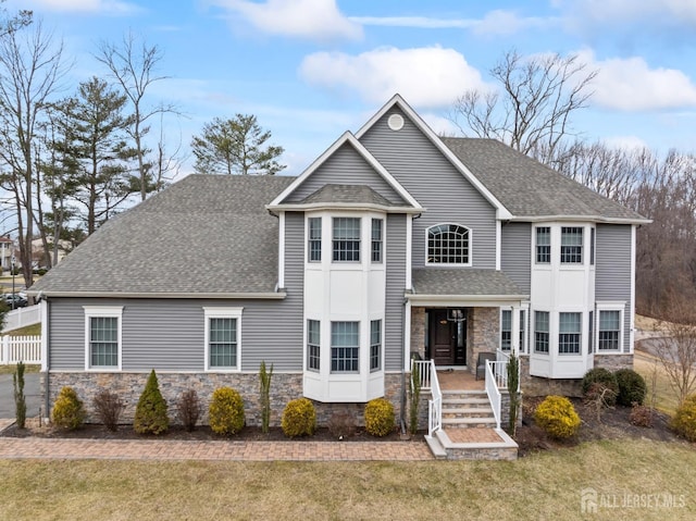 view of front of home with stone siding, fence, a front lawn, and roof with shingles