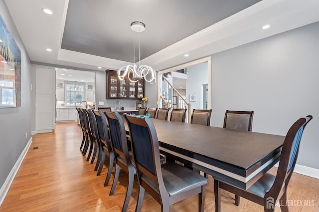 dining area featuring stairway, baseboards, light wood-type flooring, and a tray ceiling