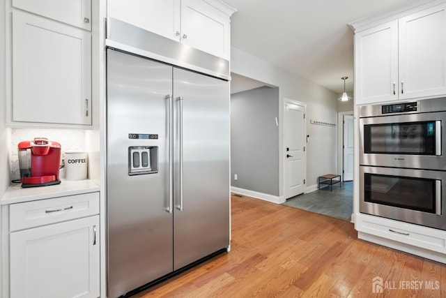 kitchen featuring light wood finished floors, white cabinets, appliances with stainless steel finishes, and tasteful backsplash