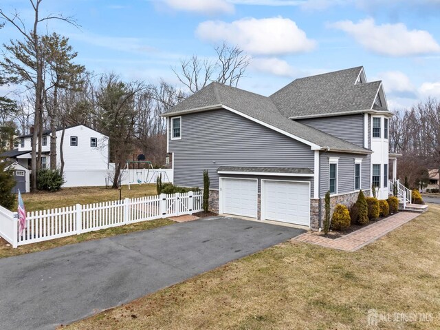 view of property exterior with aphalt driveway, stone siding, fence private yard, and roof with shingles