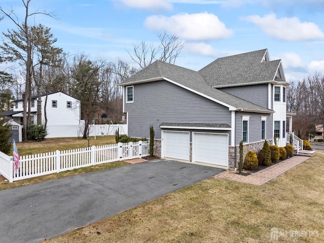 view of home's exterior featuring fence private yard, stone siding, driveway, and a shingled roof