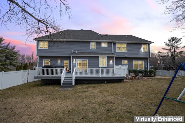 back of house at dusk featuring a yard, a wooden deck, and a fenced backyard