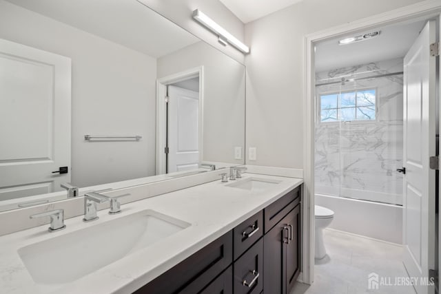 full bath with double vanity, toilet, bath / shower combo with glass door, and a sink