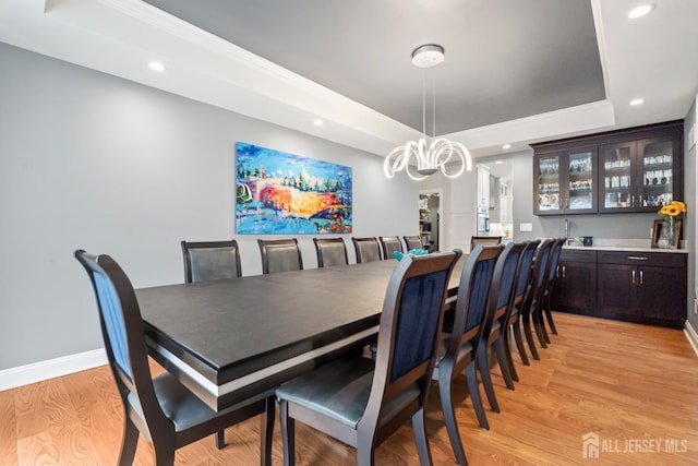 dining area featuring a tray ceiling, recessed lighting, wet bar, light wood finished floors, and baseboards