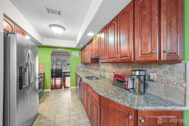 kitchen featuring light tile patterned floors, light stone counters, stainless steel appliances, a sink, and visible vents