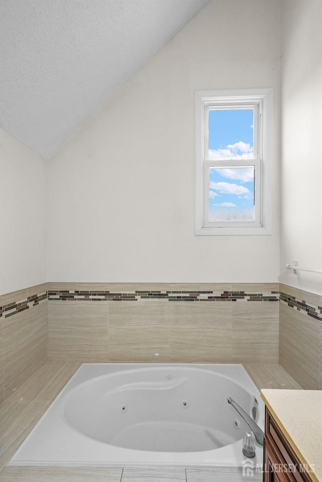 bathroom with vaulted ceiling, a tub with jets, and a textured ceiling