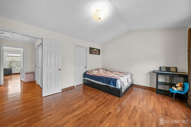 bedroom with a textured ceiling, baseboards, vaulted ceiling, light wood finished floors, and attic access