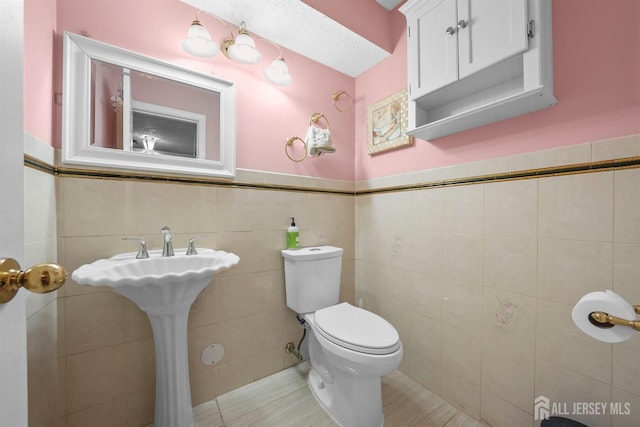 half bathroom featuring toilet, tile patterned floors, tile walls, and wainscoting