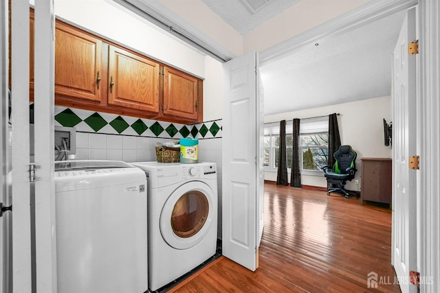 clothes washing area with visible vents, wood finished floors, washing machine and clothes dryer, and cabinet space