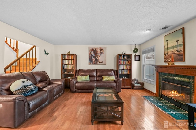 living room with visible vents, a premium fireplace, a textured ceiling, wood finished floors, and stairs