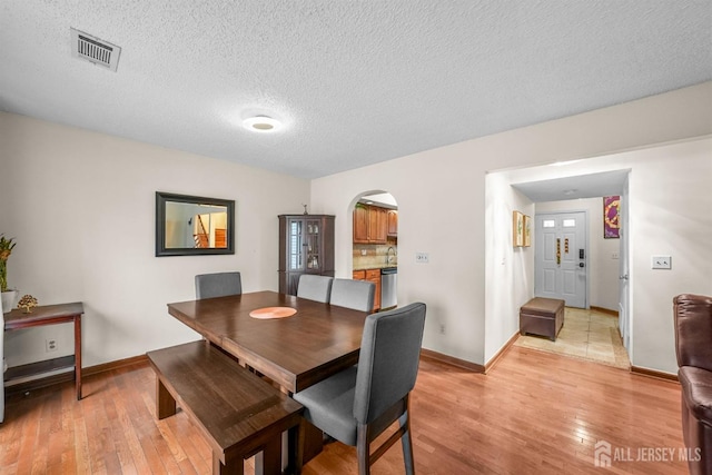 dining space featuring light wood-type flooring, visible vents, arched walkways, and a textured ceiling