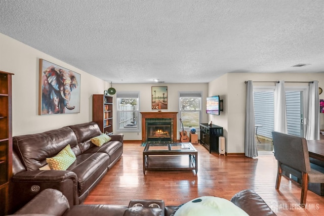 living area with baseboards, visible vents, a fireplace with flush hearth, hardwood / wood-style floors, and a textured ceiling