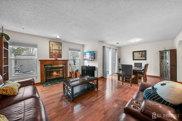 living area featuring a fireplace with flush hearth, a textured ceiling, baseboards, and wood finished floors