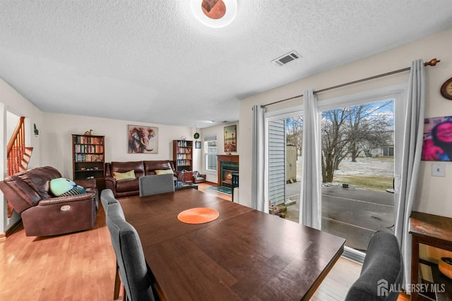 dining space with a textured ceiling, a lit fireplace, light wood-style flooring, and visible vents