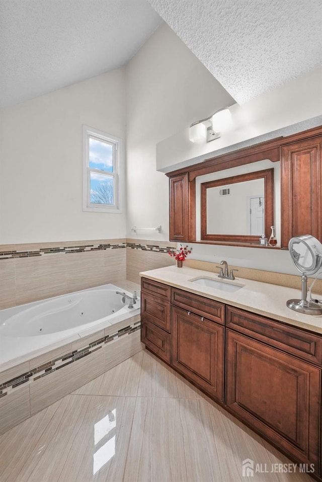 full bath featuring lofted ceiling, vanity, a textured ceiling, a whirlpool tub, and tile patterned floors