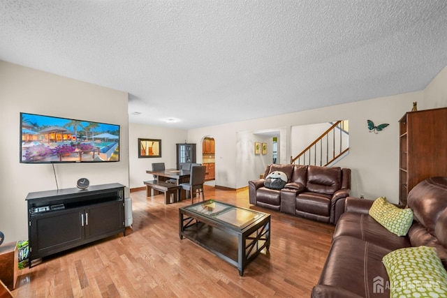 living area featuring stairway, light wood-style flooring, and a textured ceiling