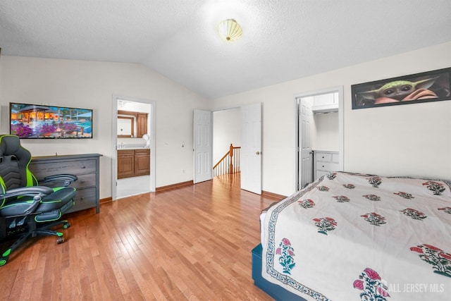 bedroom with lofted ceiling, a textured ceiling, baseboards, light wood-style floors, and ensuite bath