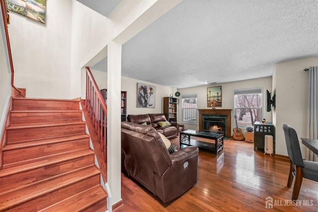 living area featuring a warm lit fireplace, a textured ceiling, hardwood / wood-style floors, and stairs