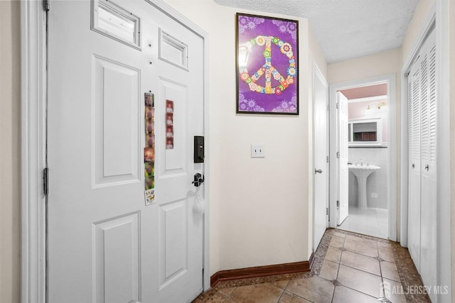 hall with tile patterned flooring, a textured ceiling, baseboards, and a sink