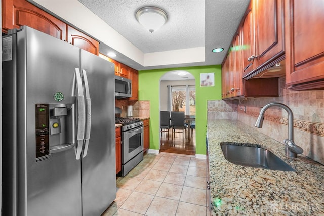 kitchen with light tile patterned floors, decorative backsplash, appliances with stainless steel finishes, a sink, and a textured ceiling