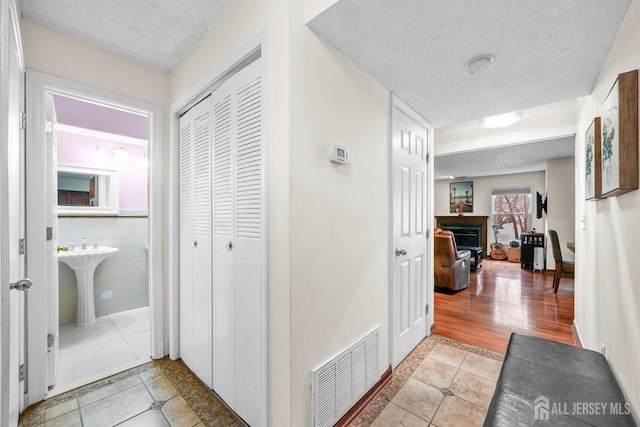 corridor featuring light tile patterned floors, a textured ceiling, a sink, and visible vents