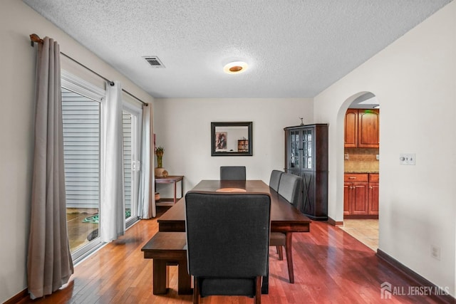 dining area with arched walkways, visible vents, a textured ceiling, and wood finished floors