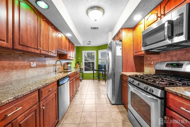 kitchen with light tile patterned floors, visible vents, light stone countertops, stainless steel appliances, and a sink