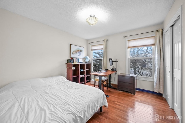 bedroom with a textured ceiling, a closet, wood-type flooring, and baseboards