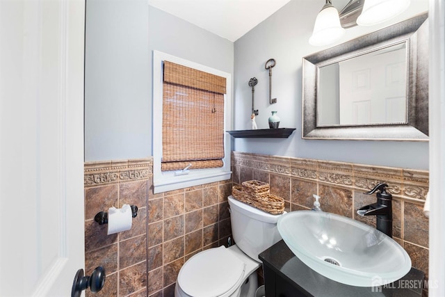 half bath with vanity, a wainscoted wall, toilet, and tile walls