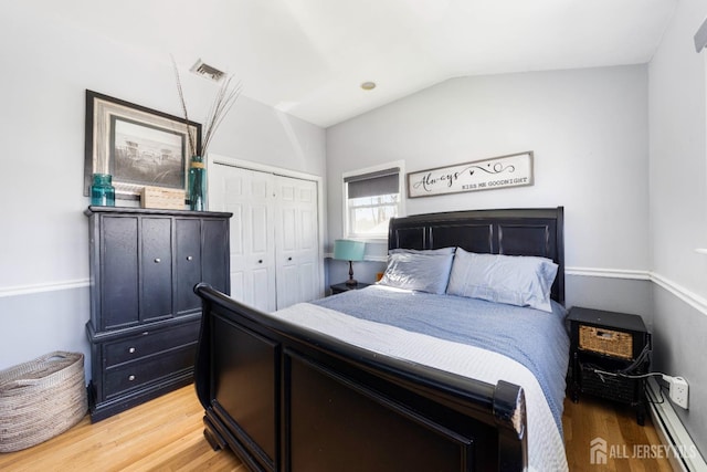 bedroom featuring visible vents, a closet, lofted ceiling, baseboard heating, and light wood-type flooring