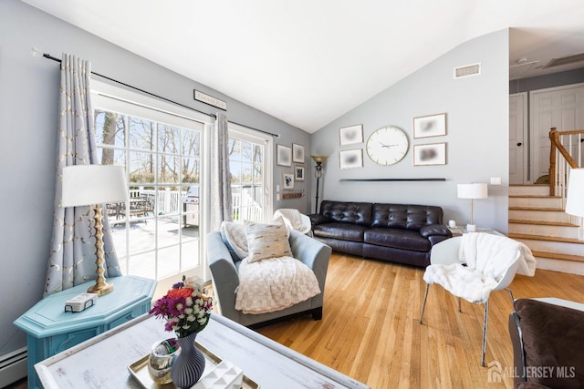living area featuring visible vents, baseboard heating, vaulted ceiling, wood finished floors, and stairway