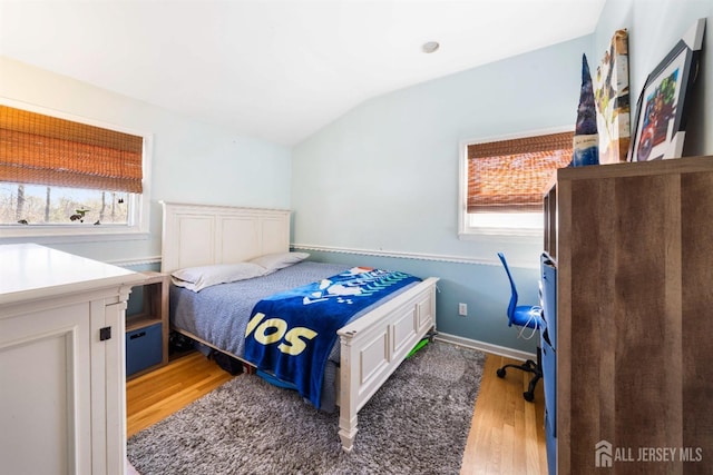 bedroom with baseboards, light wood-style flooring, vaulted ceiling, and multiple windows