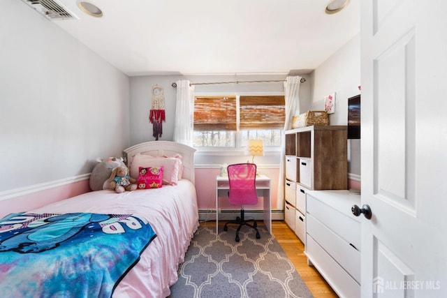 bedroom with light wood-style floors, a baseboard heating unit, and visible vents