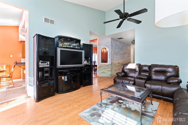 living room featuring light wood finished floors, a towering ceiling, visible vents, and a ceiling fan