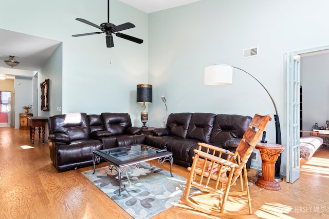 living area featuring a ceiling fan, visible vents, a high ceiling, and wood finished floors