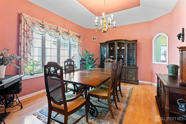 dining room featuring light wood-type flooring, baseboards, visible vents, and a tray ceiling