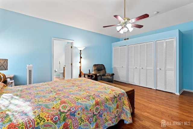 bedroom with ceiling fan, wood finished floors, visible vents, two closets, and ensuite bath