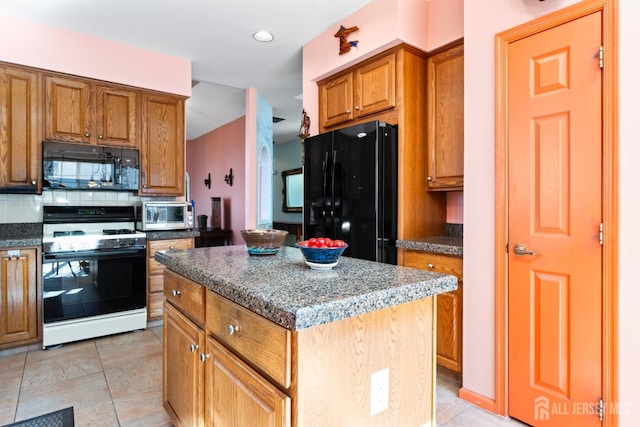 kitchen with brown cabinetry, dark stone countertops, a center island, black appliances, and backsplash