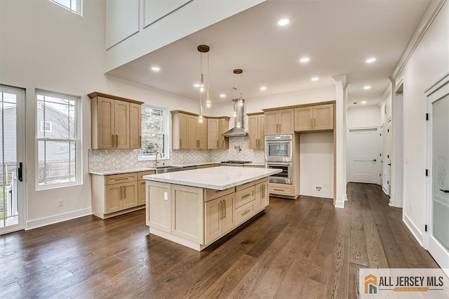 kitchen featuring sink, a kitchen island, wall chimney range hood, light brown cabinetry, and hanging light fixtures